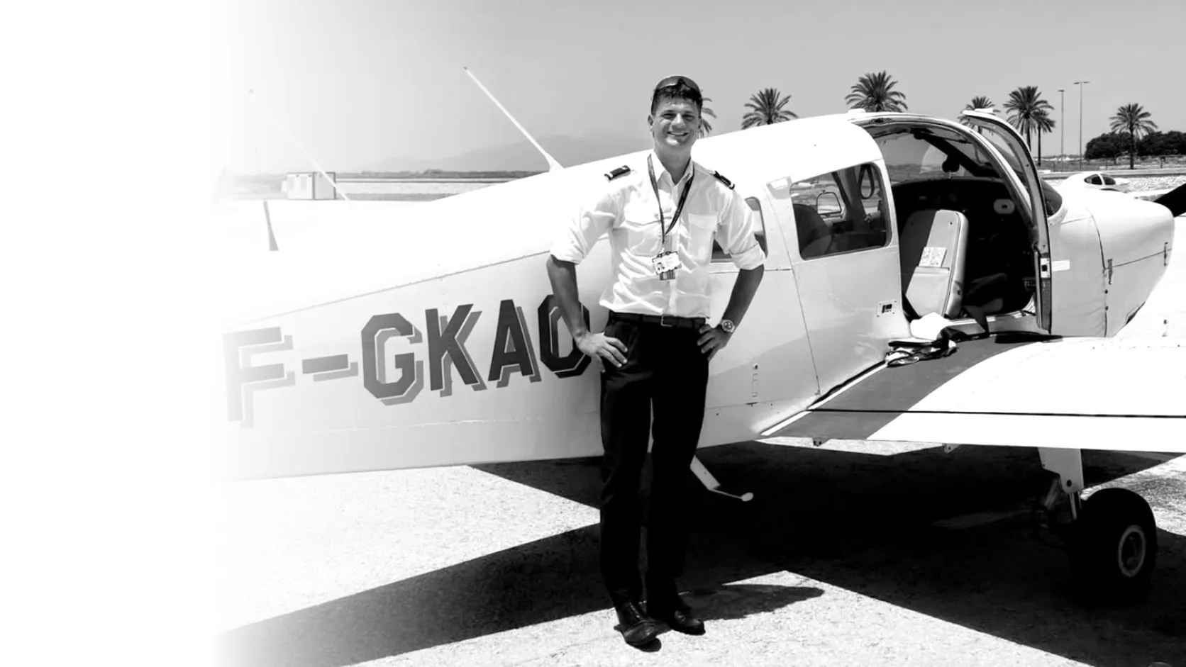 Charlie in pilot uniform, leaning against a Piper training aircraft on the apron